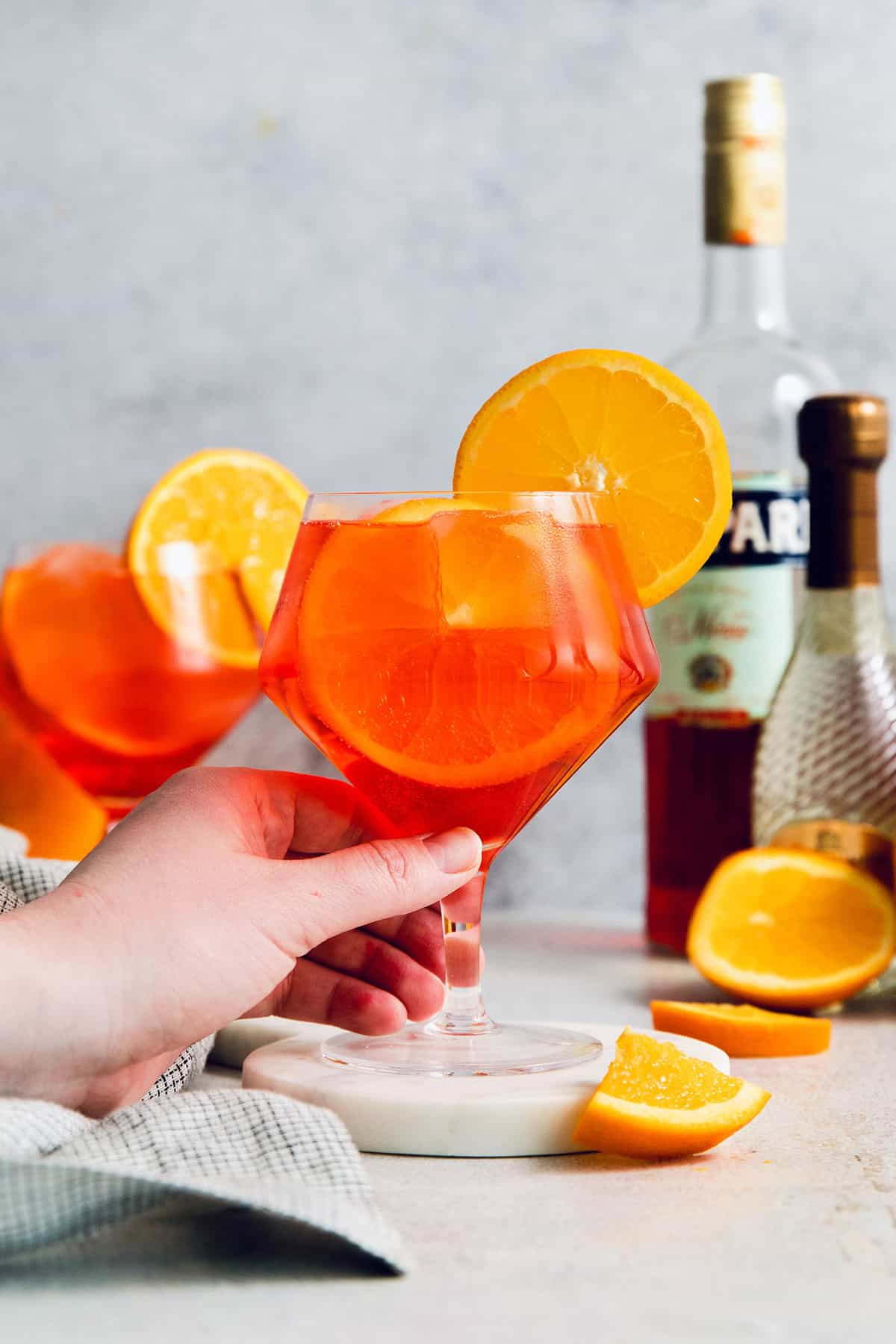 This refreshing, ruby-red Campari Spritz is a beautifully simple drink made with just 3 ingredients including campari and Prosecco. a hand holding a Campari spritz cocktail