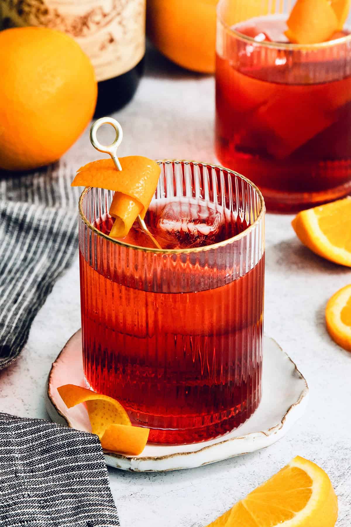 This classic Italian Negroni recipe features an easy 1-1-1 ratio of gin, Campari, and sweet vermouth and is served over ice. A Negroni is served with orange peel on a white plate.