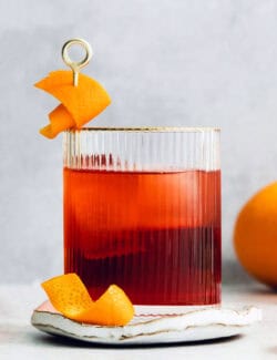 A beautiful red Negroni in a cocktail glass with orange peels.