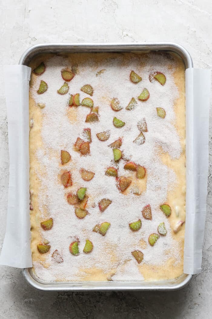 rhubarb coffee cake batter in a 9x13 pan, with sugar and rhubarb pieces scattered over the top