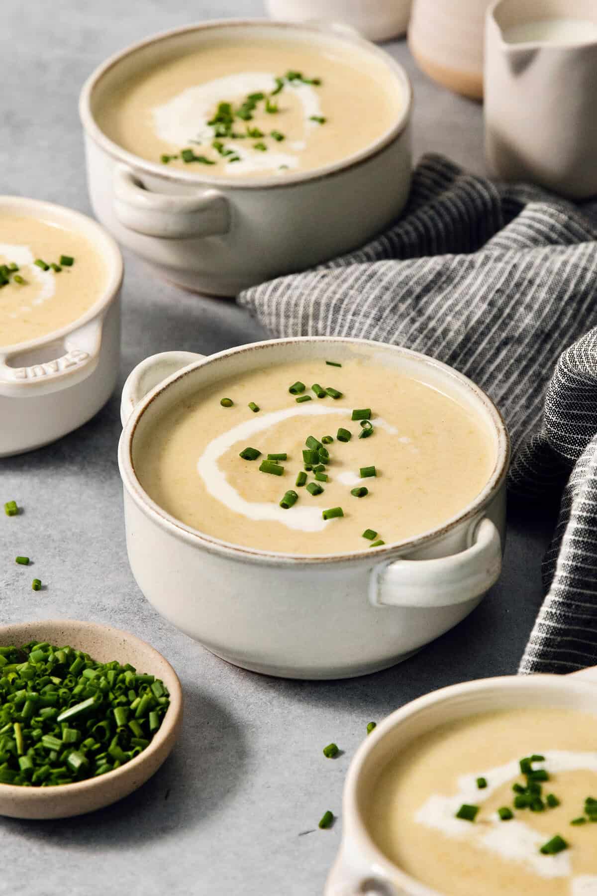 Bowls of vichyssoise are served with a bowl of chives next to them.