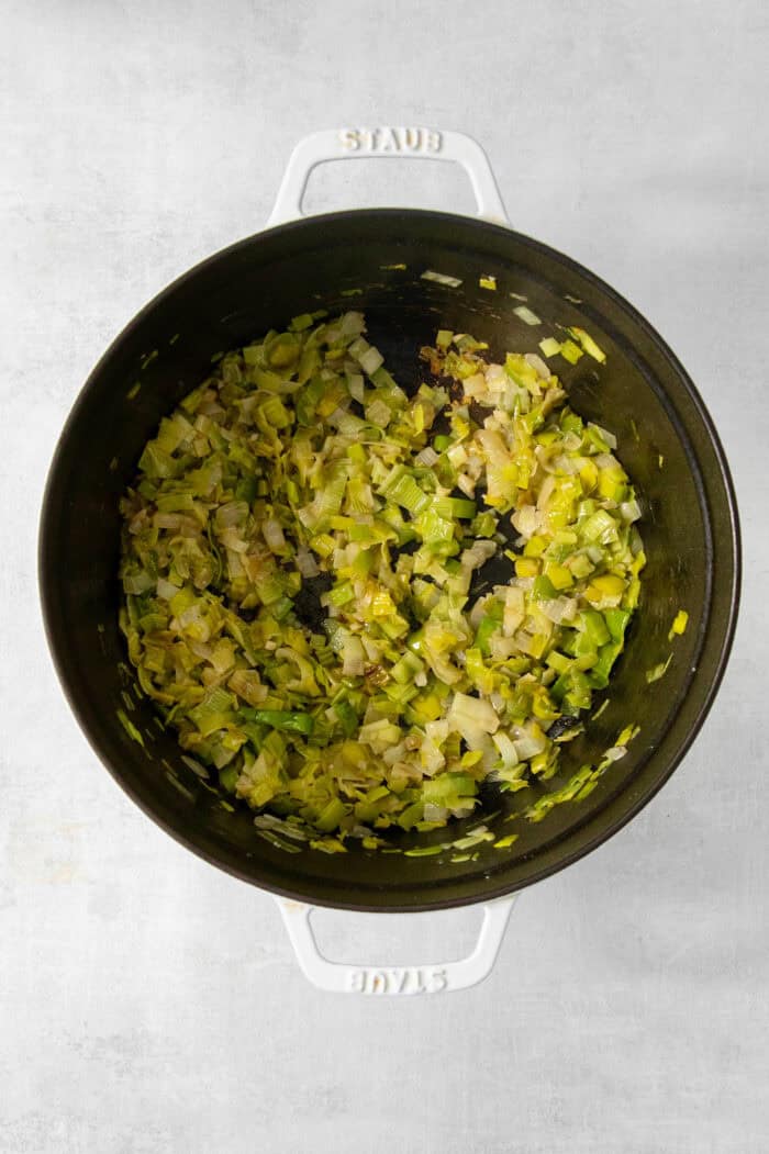 Onions, garlic, and leek are cooked in a pot.