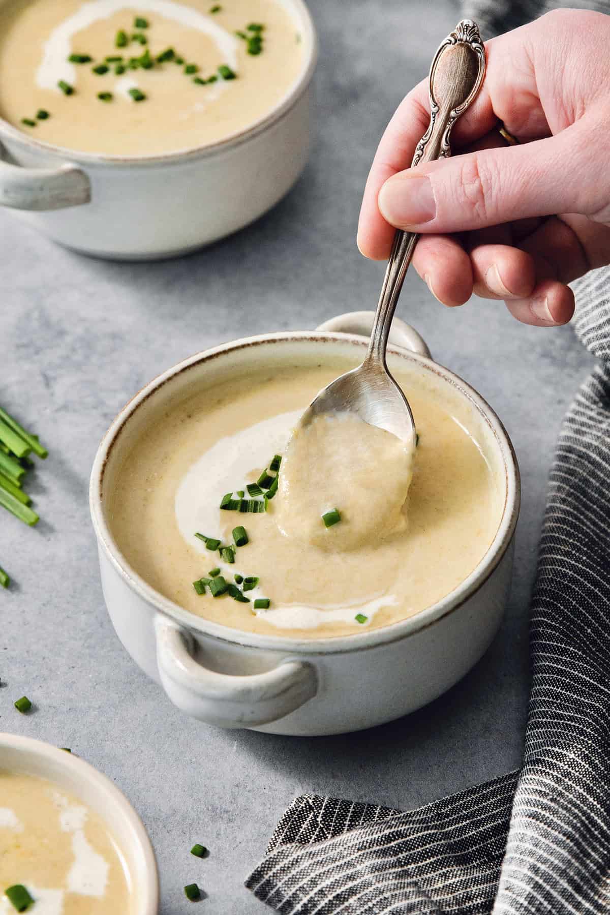 A hand dips a spoon into a bowl of vichyssoise.