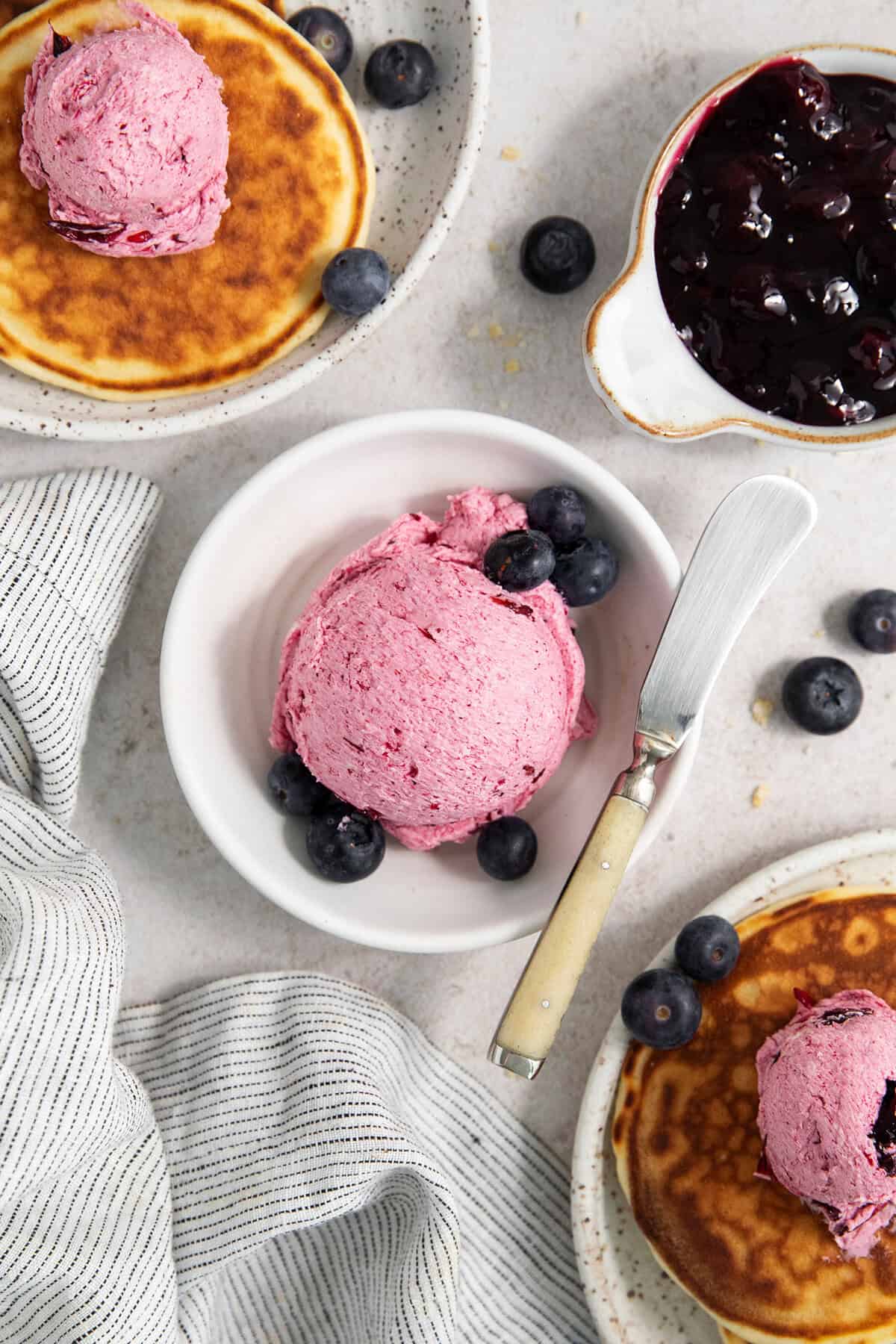 This Blueberry Butter is lightly sweet and luxuriously fluffy, with an easy homemade fresh blueberry sauce as its base. Pancakes on plates topped with blueberry butter and a bowl of blueberry butter.