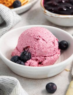 A white bowl holds a big scoop of blueberry butter with fresh bluberries around it.