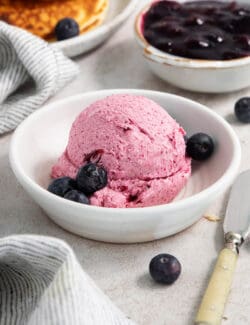 A white bowl holds a big scoop of blueberry butter with fresh bluberries around it.