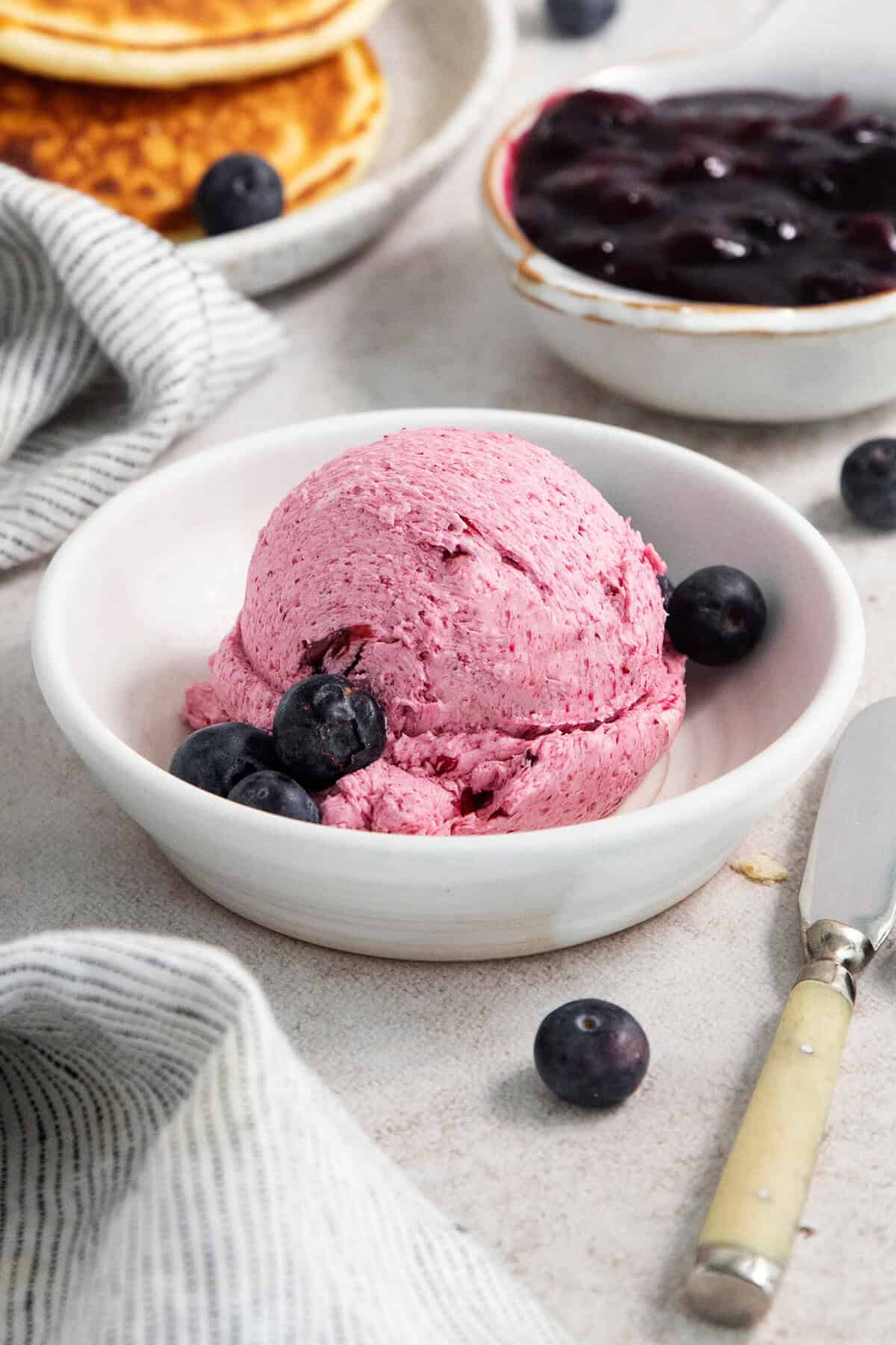 This Blueberry Butter is lightly sweet and luxuriously fluffy, with an easy homemade fresh blueberry sauce as its base. A white bowl holds a big scoop of blueberry butter with fresh bluberries around it.