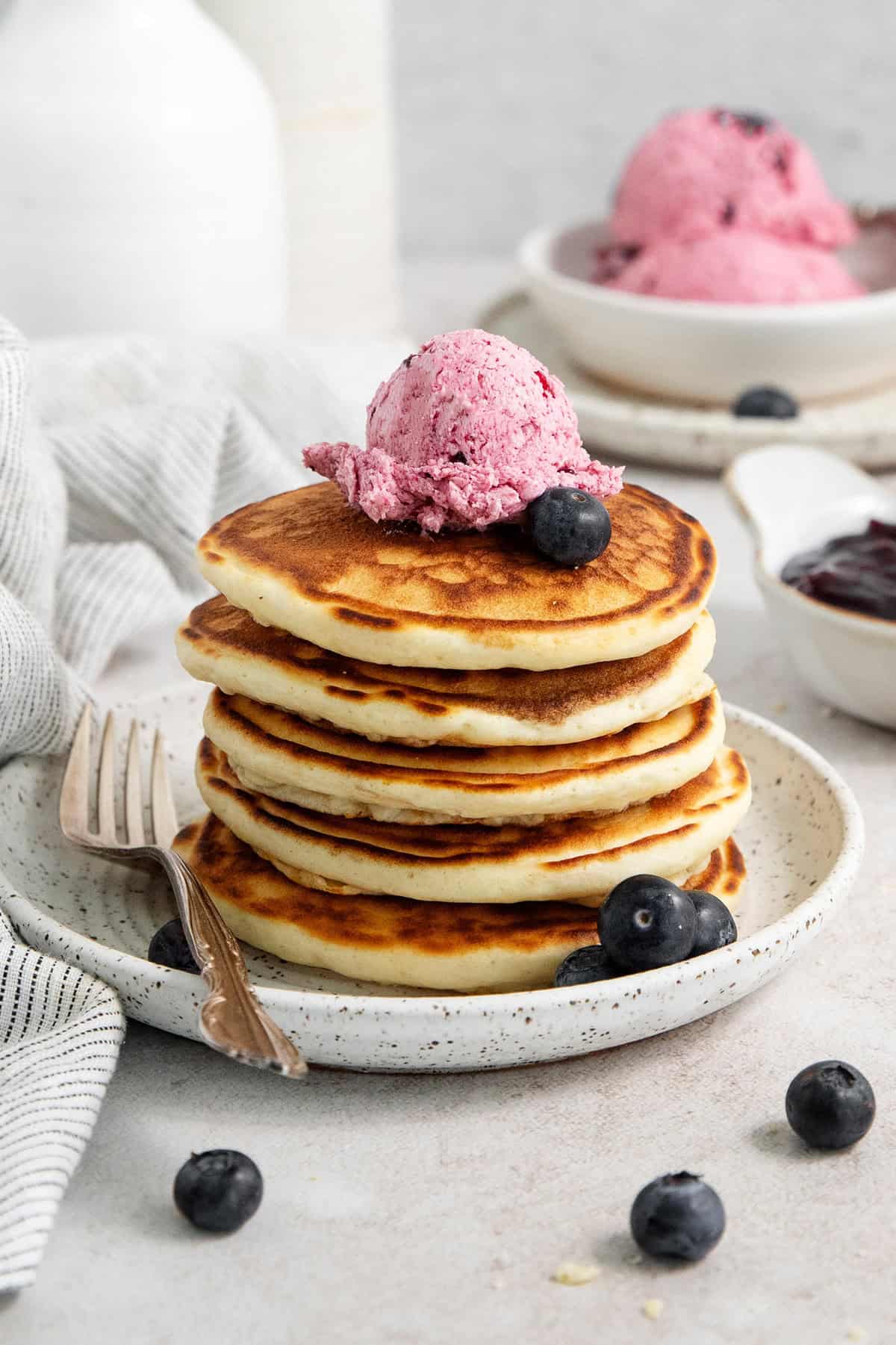 This Blueberry Butter is lightly sweet and luxuriously fluffy, with an easy homemade fresh blueberry sauce as its base. A stack of pancakes on a plate is topped with blueberry butter.