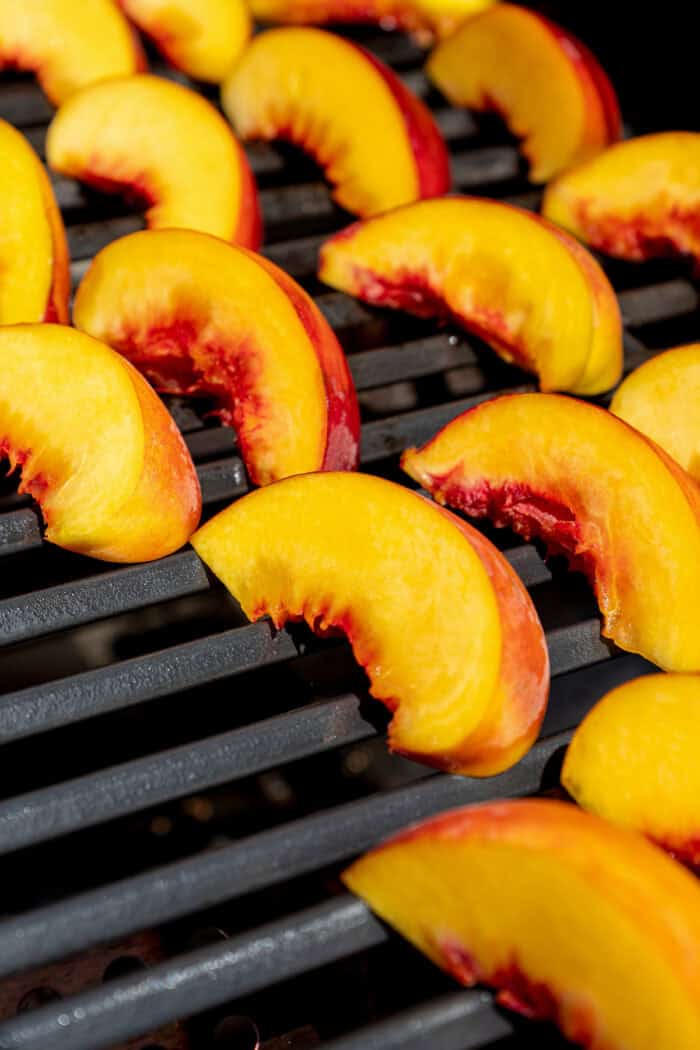 Sweet and juicy Grilled Peach Salad features lightly grilled peaches served with greens, cherry tomatoes, and fresh mozzarella. Peach slices are placed on a grill.