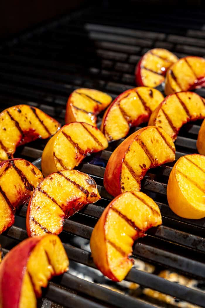 Sweet and juicy Grilled Peach Salad features lightly grilled peaches served with greens, cherry tomatoes, and fresh mozzarella. Peach slices cook on the grill with char marks visible.