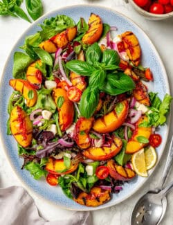Basil leaves top a colorful serving platter of grilled peach salad.