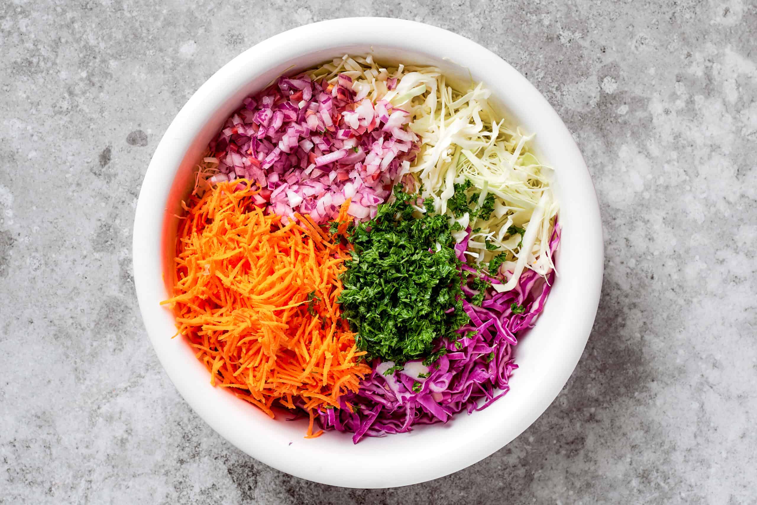 This jalapeño slaw recipe features a crunchy mix of vegetables including cabbage, cilantro, and carrots tossed in a lightly sweet dressing. jalapeno slaw mix in a white bowl