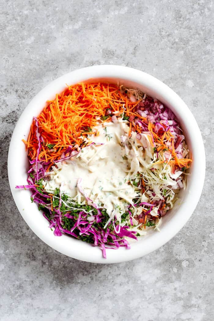 This jalapeño slaw recipe features a crunchy mix of vegetables including cabbage, cilantro, and carrots tossed in a lightly sweet dressing. jalapeno slaw mix and dressing in a white bowl