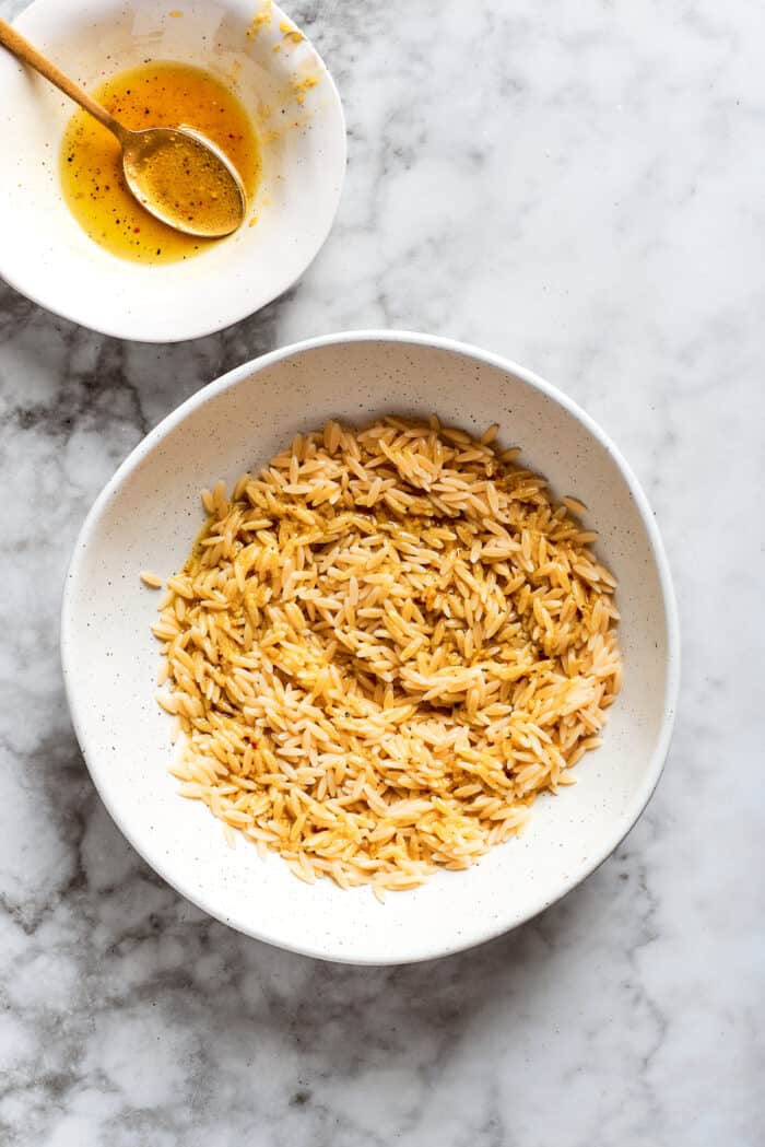 This easy Lemon Chicken Orzo Salad features fresh veggies, chicken, pasta, and a tangy lemon vinaigrette for a light yet filling meal. Orzo in a bowl with a bowl of dressing next to it.