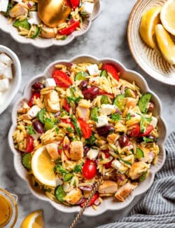 a serving spoon in a white bowl full of lemon orzo salad with chicken