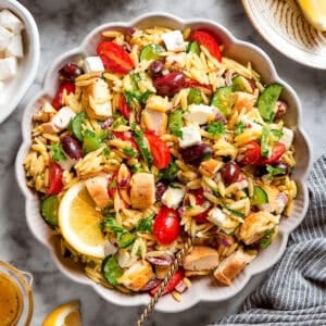 a serving spoon in a white bowl full of orzo salad