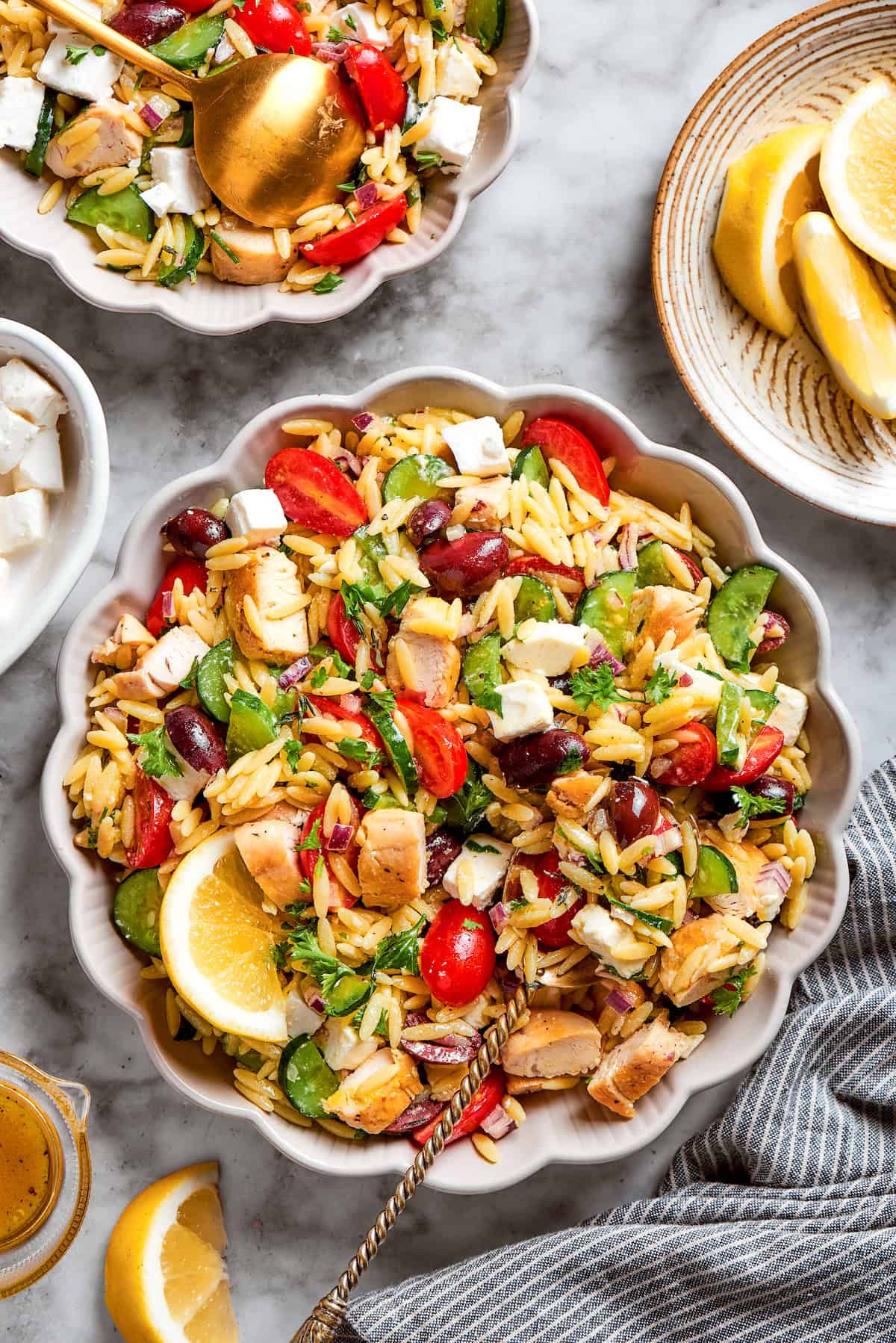 This easy Lemon Chicken Orzo Salad features fresh veggies, chicken, pasta, and a tangy lemon vinaigrette for a light yet filling meal. a serving spoon in a white bowl full of lemon orzo salad with chicken
