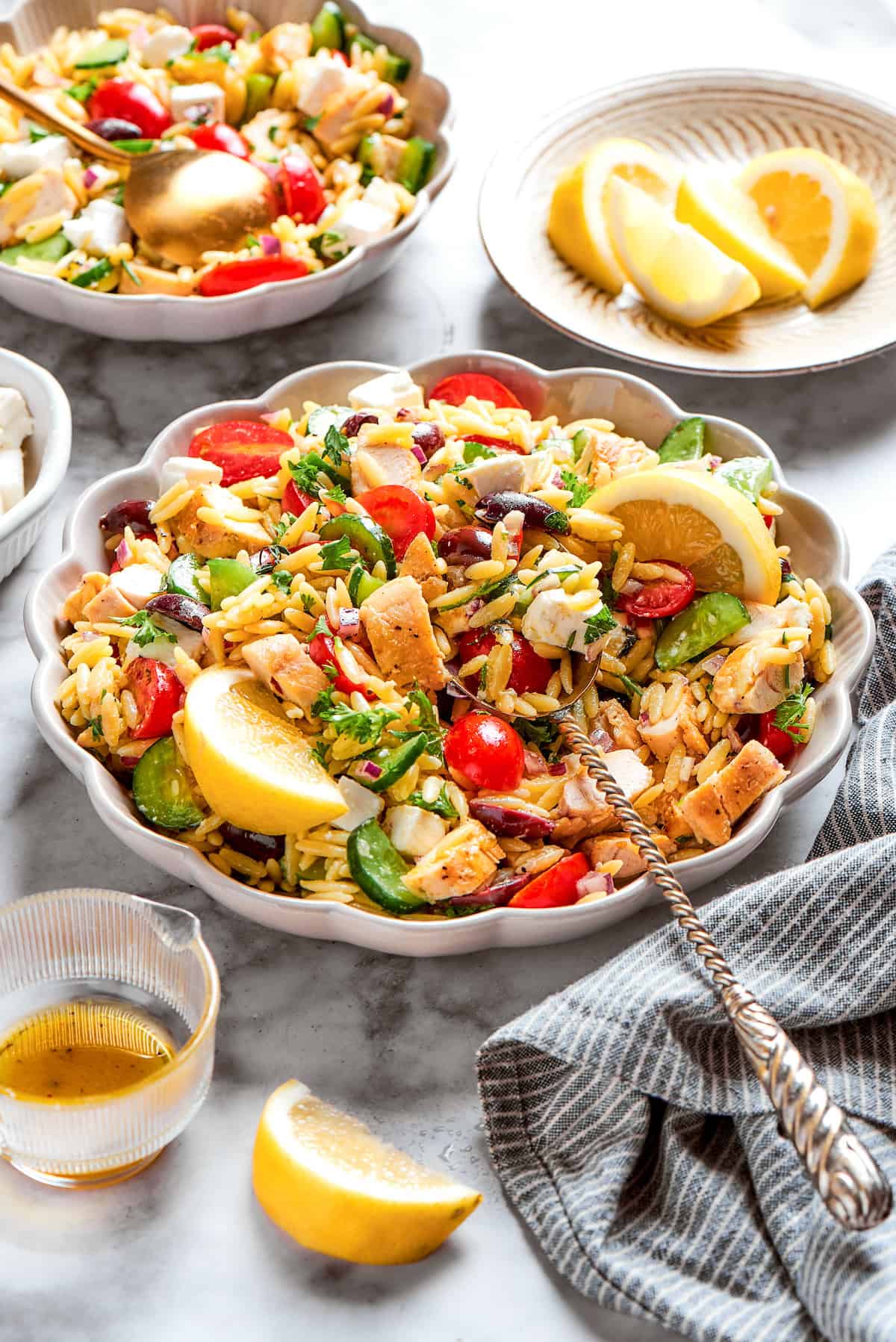This easy Lemon Chicken Orzo Salad features fresh veggies, chicken, pasta, and a tangy lemon vinaigrette for a light yet filling meal. A serving bowl of lemon chicken orzo salad with lemon wedges on a table.