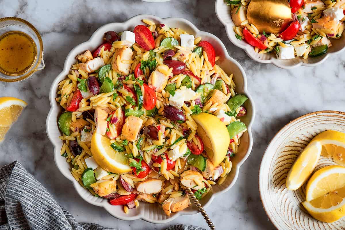 a serving spoon in a white bowl full of orzo chicken salad with lemon