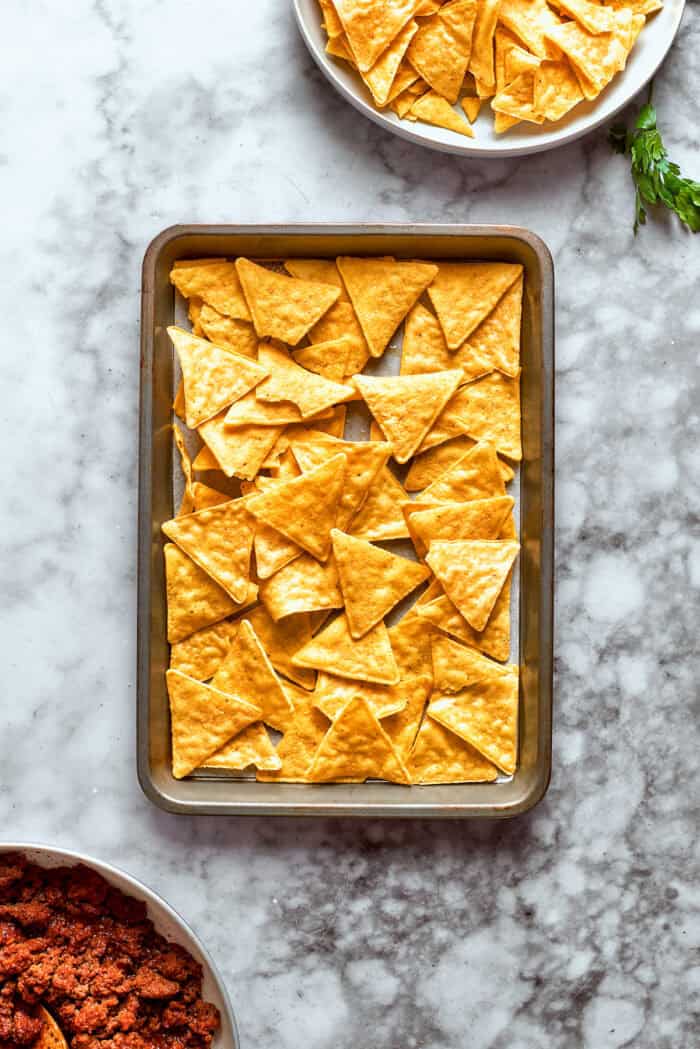 This Macho Nachos recipe features layers of crispy tortilla chips, melty cheese, and seasoned beef. Perfect for any casual gathering! Chips are added to a sheet pan.