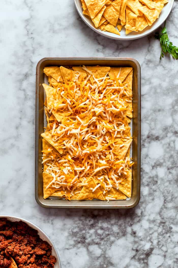 This Macho Nachos recipe features layers of crispy tortilla chips, melty cheese, and seasoned beef. Perfect for any casual gathering! Cheese is added to the first layer of chips.