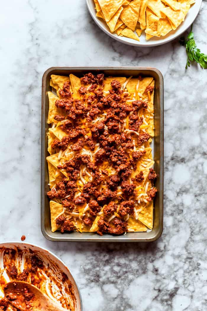 This Macho Nachos recipe features layers of crispy tortilla chips, melty cheese, and seasoned beef. Perfect for any casual gathering! Meat is piled on the chips.