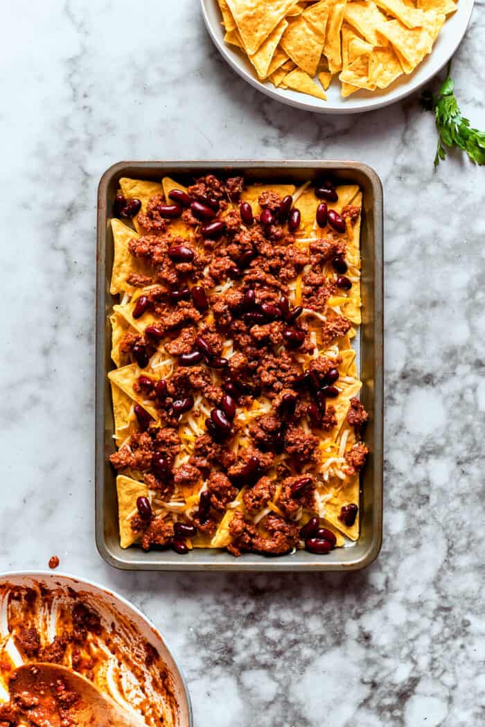 This Macho Nachos recipe features layers of crispy tortilla chips, melty cheese, and seasoned beef. Perfect for any casual gathering! Black beans are added to the chips and meat.