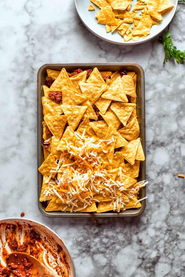 This Macho Nachos recipe features layers of crispy tortilla chips, melty cheese, and seasoned beef. Perfect for any casual gathering! More chips and cheese are added to the beans and meat.