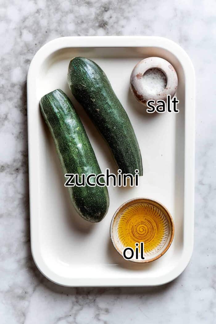 zucchini, oil, and salt on a white rimmed pan