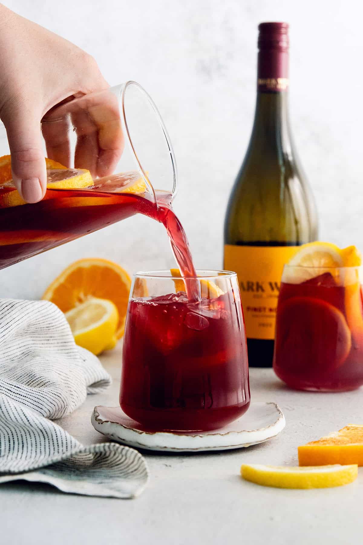 Tinto de Verano, a Spanish summertime cocktail, features fruity red wine, lemon soda, and red vermouth served over ice. A hand pours tinto de verano from a pitcher in a glass.