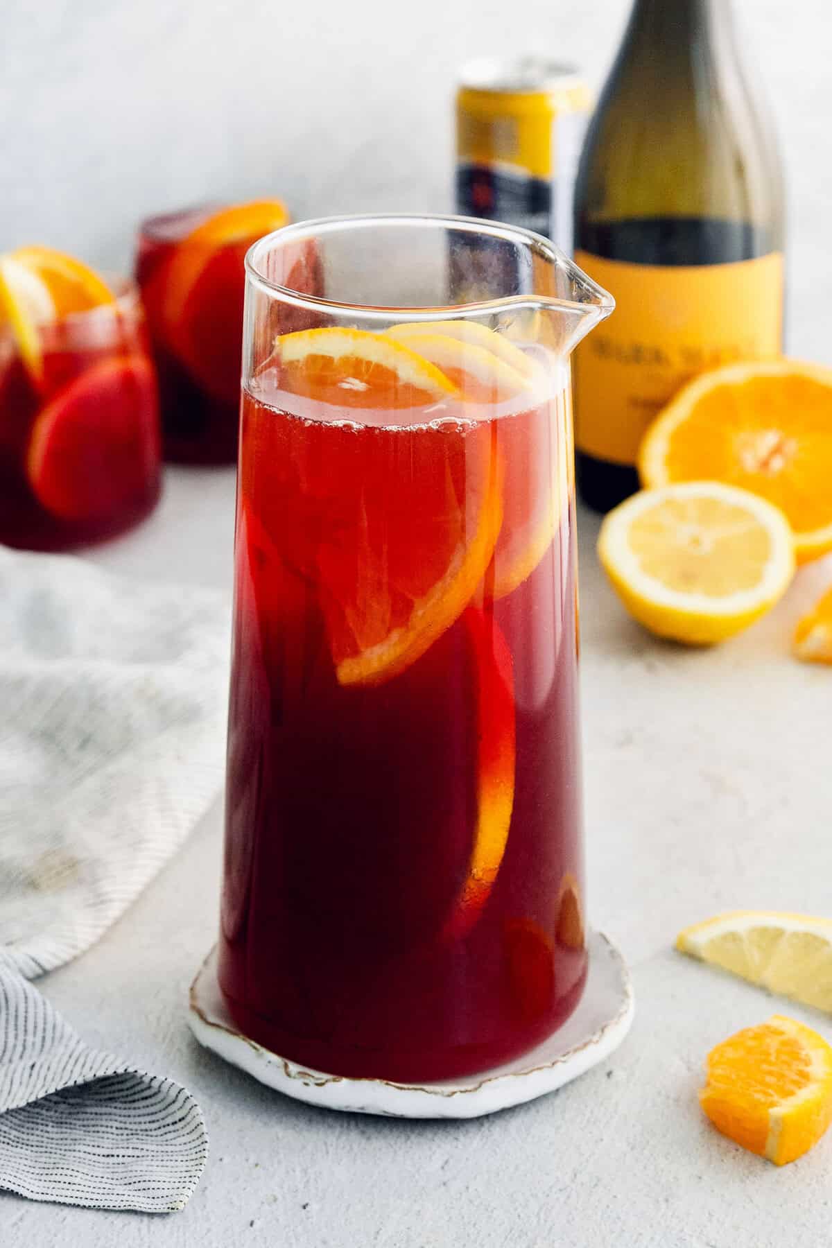 Tinto de Verano, a Spanish summertime cocktail, features fruity red wine, lemon soda, and red vermouth served over ice. A glass pitcher full of tinto de verano and lemon and orange slices.