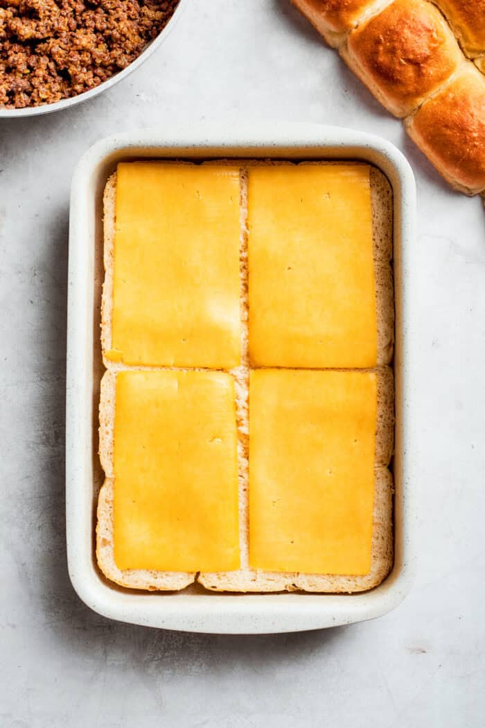 Homemade Cheeseburger Sliders star tender ground beef topped with plenty of melted cheddar cheese served on sweet rolls. Sliced cheese is placed on top of sliced rolls.