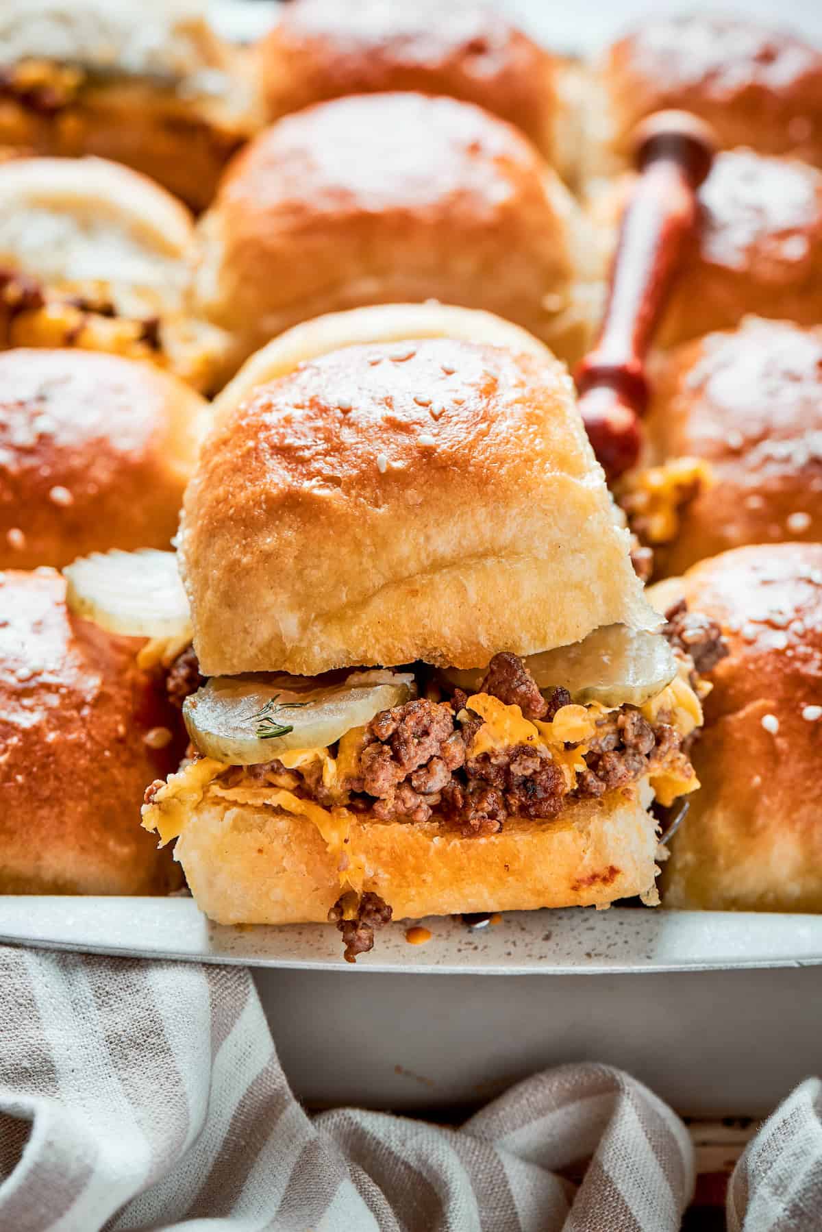 Homemade Cheeseburger Sliders star tender ground beef topped with plenty of melted cheddar cheese served on sweet rolls. A bun tops a cheeseburger slider.