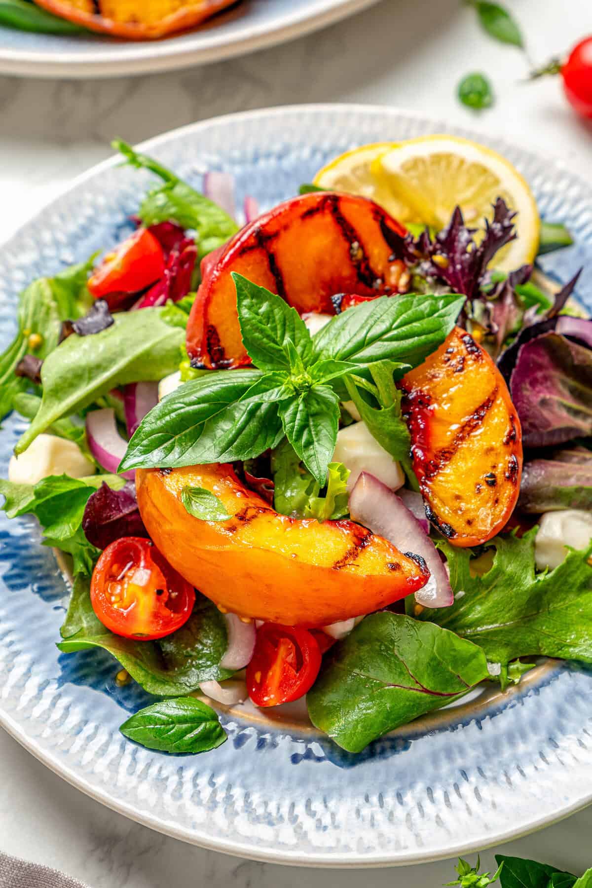 Sweet and juicy Grilled Peach Salad features lightly grilled peaches served with greens, cherry tomatoes, and fresh mozzarella. an individual plate of salad with grilled peaches and basil