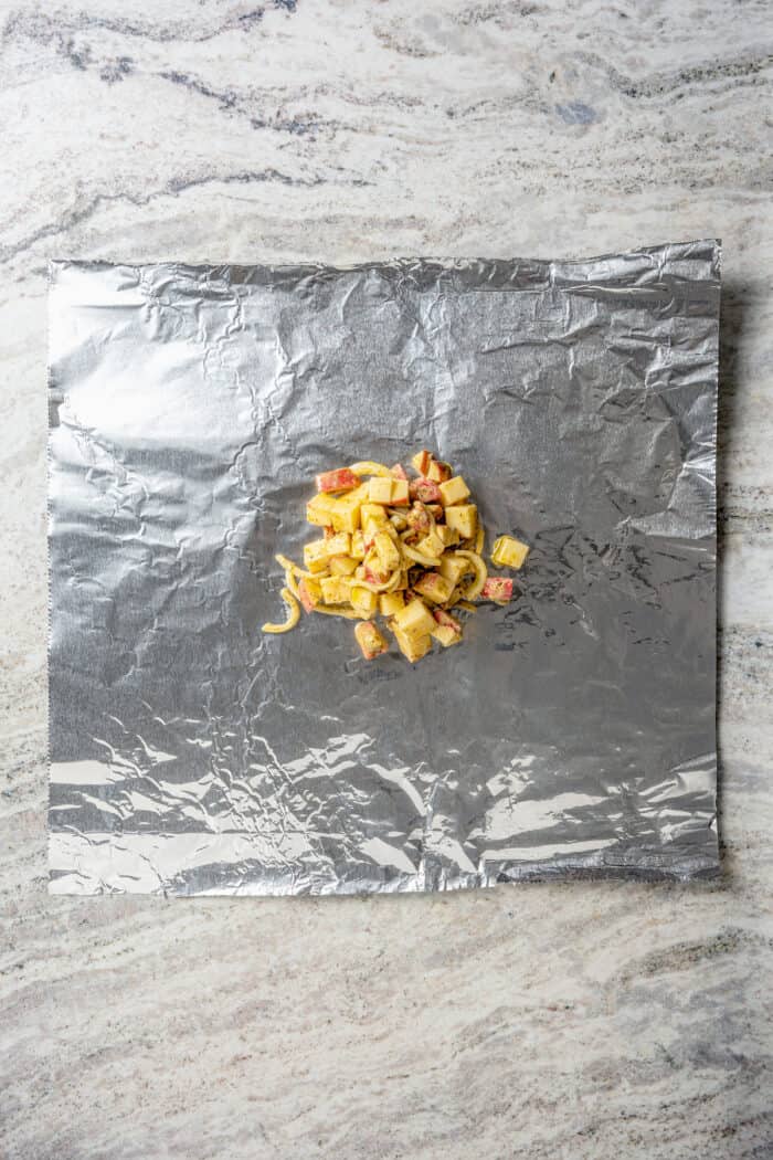 Savory Grilled Potato Packets feature grilled potatoes in foil dressed in tangy, garlicky pesto-ranch sauce and ready in less than 30 minutes. Potato pieces are placed in the middle of a piece of foil.