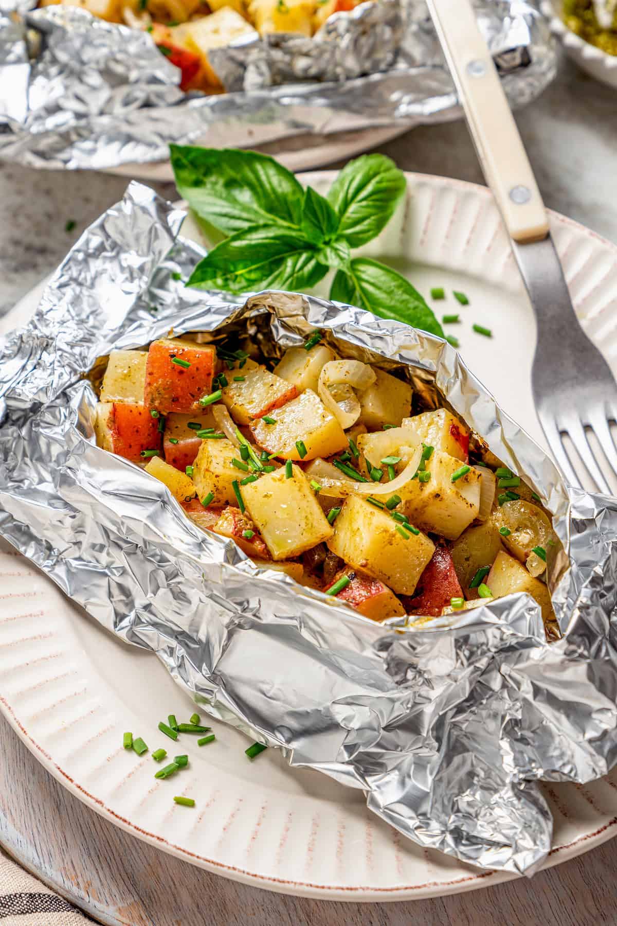 Savory Grilled Potato Packets feature grilled potatoes in foil dressed in tangy, garlicky pesto-ranch sauce and ready in less than 30 minutes. A grilled potato packet is opened to show the cooked potatoes inside.