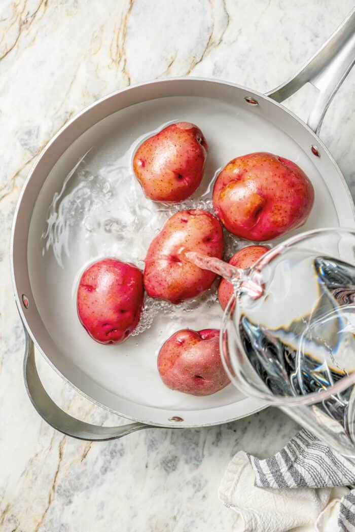 Crisp-tender Grilled Red Potatoes are spiked with the brisk flavors of dill, feta cheese, and lemon and grilled to perfection. Water is added to red potatoes in a pot.
