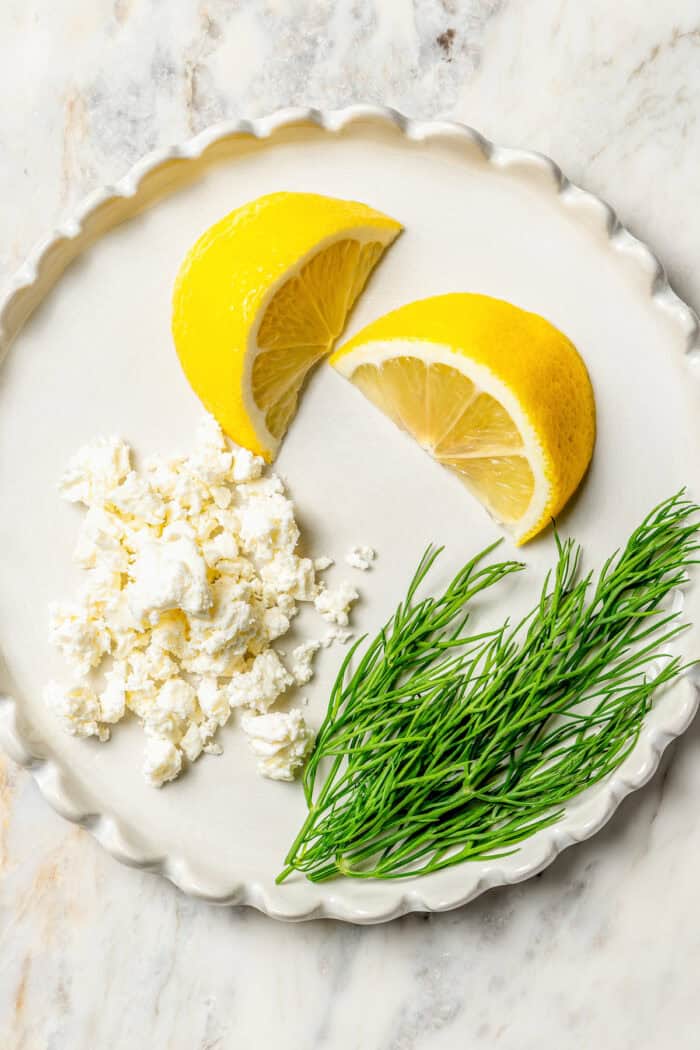 Crisp-tender Grilled Red Potatoes are spiked with the brisk flavors of dill, feta cheese, and lemon and grilled to perfection. Lemon wedges, feta, and dill on a p late.