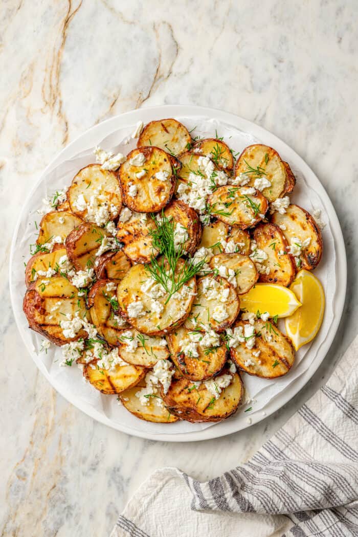 Crisp-tender Grilled Red Potatoes are spiked with the brisk flavors of dill, feta cheese, and lemon and grilled to perfection. A plate of grilled red potatoes with lemon, feta, and dill.