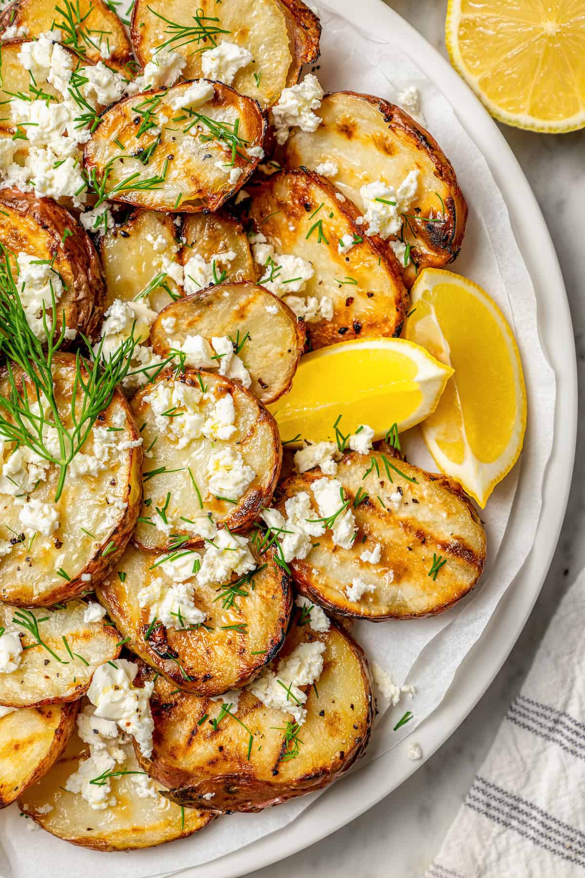 Crisp-tender Grilled Red Potatoes are spiked with the brisk flavors of dill, feta cheese, and lemon and grilled to perfection. Lemon wedges are tucked in between sliced of grilled red potatoes.