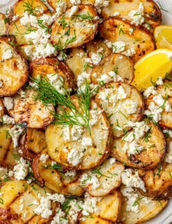Flecks of feta cheese and sprigs of fresh dil ltop a plate of grilled red potatoes.