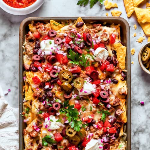 overhead photo of a rimmed pan full of baked cheesy nachos loaded with meat and vegetables