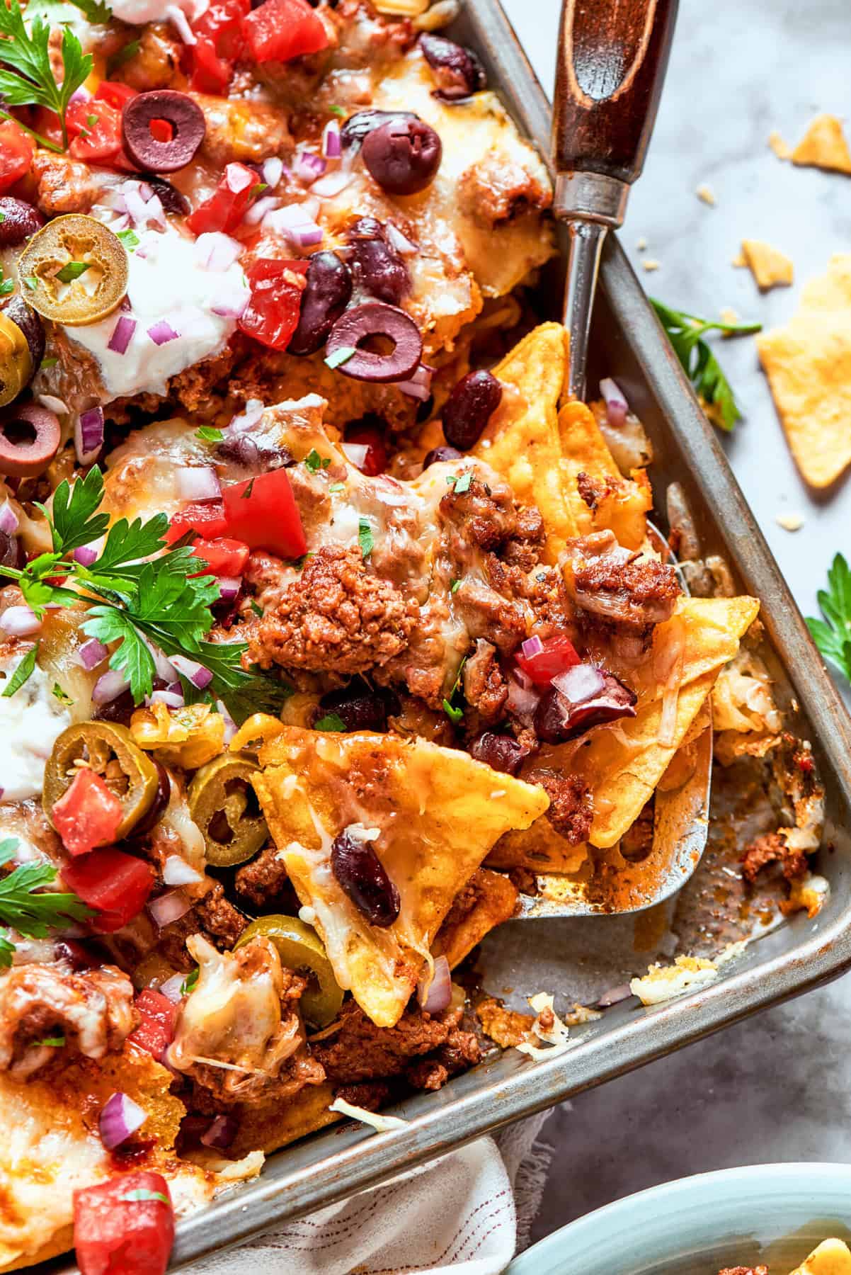 This Macho Nachos recipe features layers of crispy tortilla chips, melty cheese, and seasoned beef. Perfect for any casual gathering! a rimmed pan of macho nachos with a spatula in it
