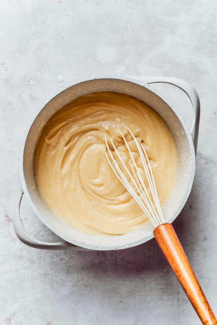 Rømmegrøt is a warmed Norwegian porridge similar to rich pudding, served with a drizzle of melted butter and a good sprinkling of cinnamon! A whisk stirs a pot of thick Rømmegrøt.