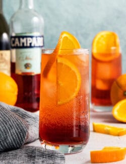 A bottle of Campari stands in the background with two Americano cocktails.