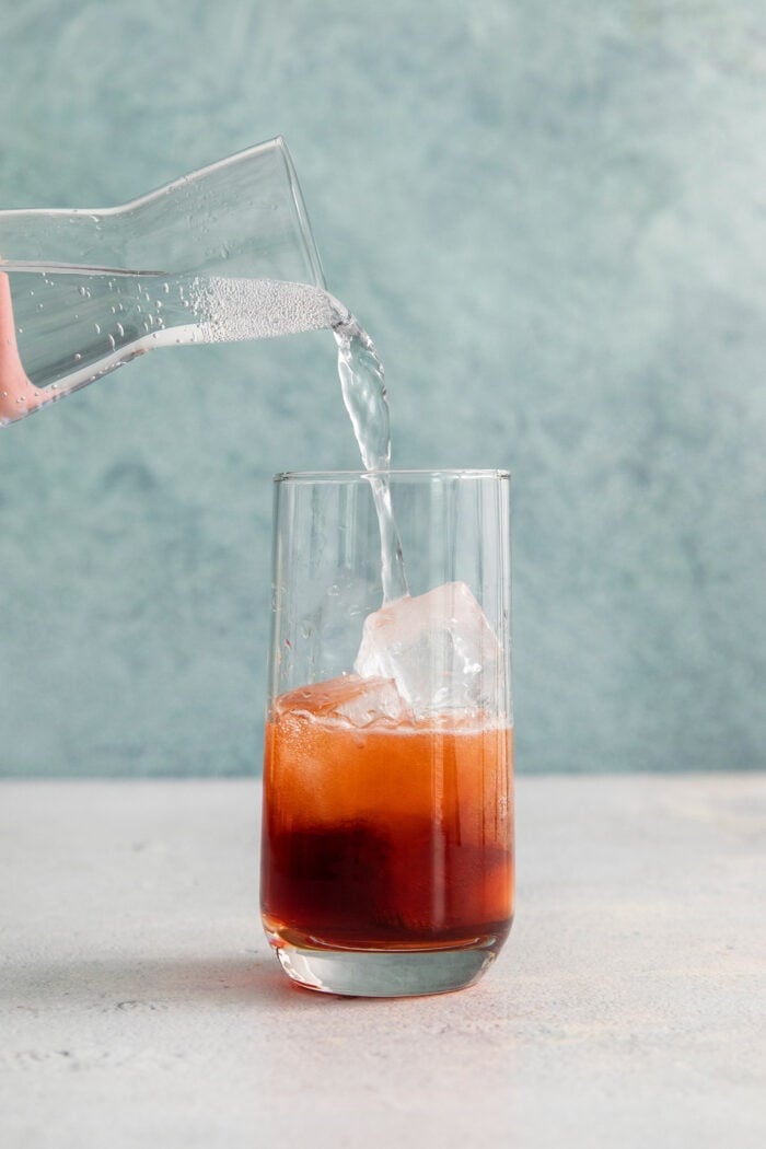 This 3-ingredient Americano Cocktail is made from equal parts Campari and sweet vermouth plus a splash of bubbly club soda. Soda water is added to a glass of Americano cocktail.