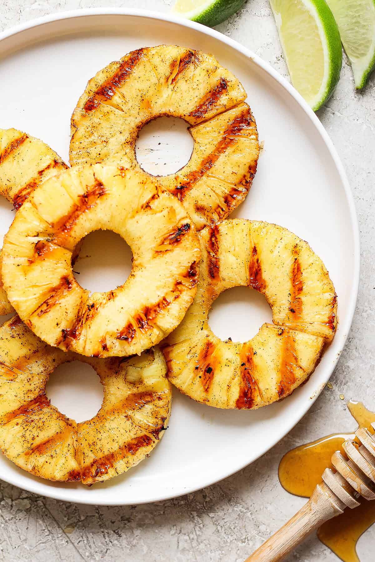 Lightly caramelized and so juicy Grilled Pineapple is a blend of sweet and spicy, perfect on top of burgers or as a dessert. Pineapple rings with char marks after being grilled, on a plate.