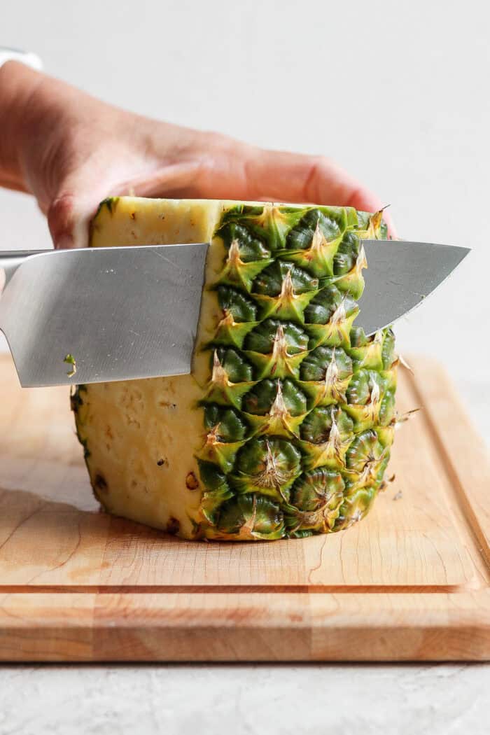 Lightly caramelized and so juicy Grilled Pineapple is a blend of sweet and spicy, perfect on top of burgers or as a dessert. A pineapple is held upright while a knife is used to cut off the skin.