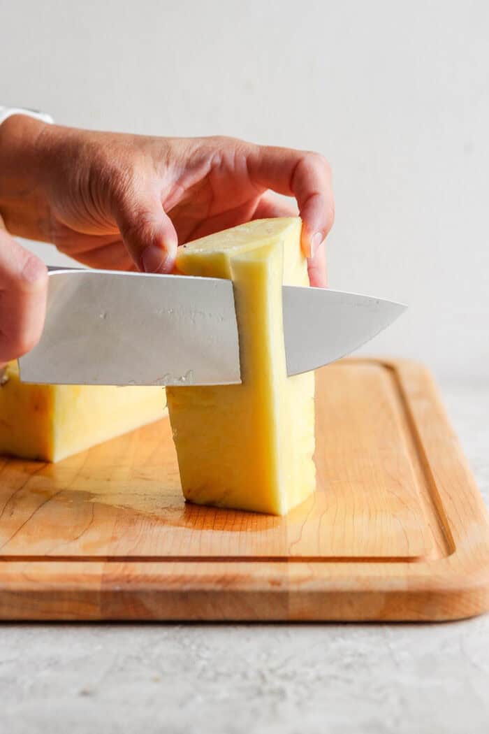 Lightly caramelized and so juicy Grilled Pineapple is a blend of sweet and spicy, perfect on top of burgers or as a dessert. A knife slices through pineapple.