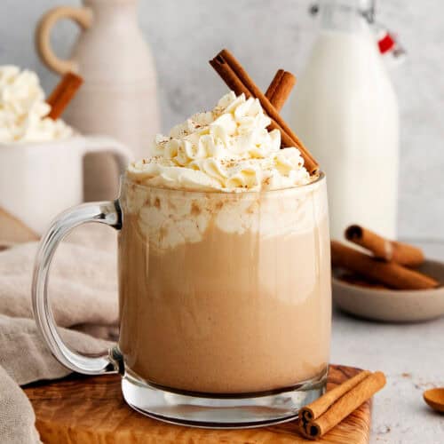 Mugs of pumpkin spice latte are garnished with cinnamon sticks and topped with whipped cream.